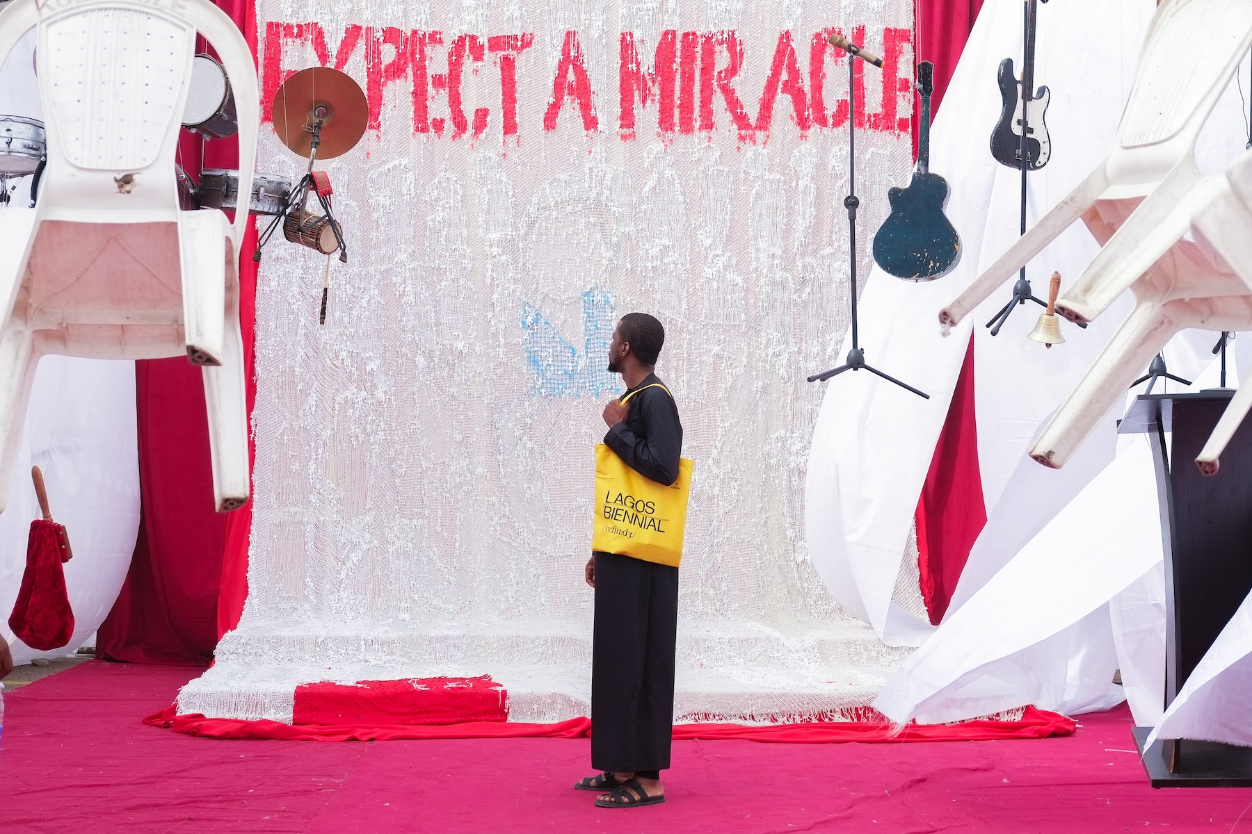 Victor Ehikhamenor’s Miracle Central installation at the 2024 Lagos Biennial, with suspended chairs and a red aisle